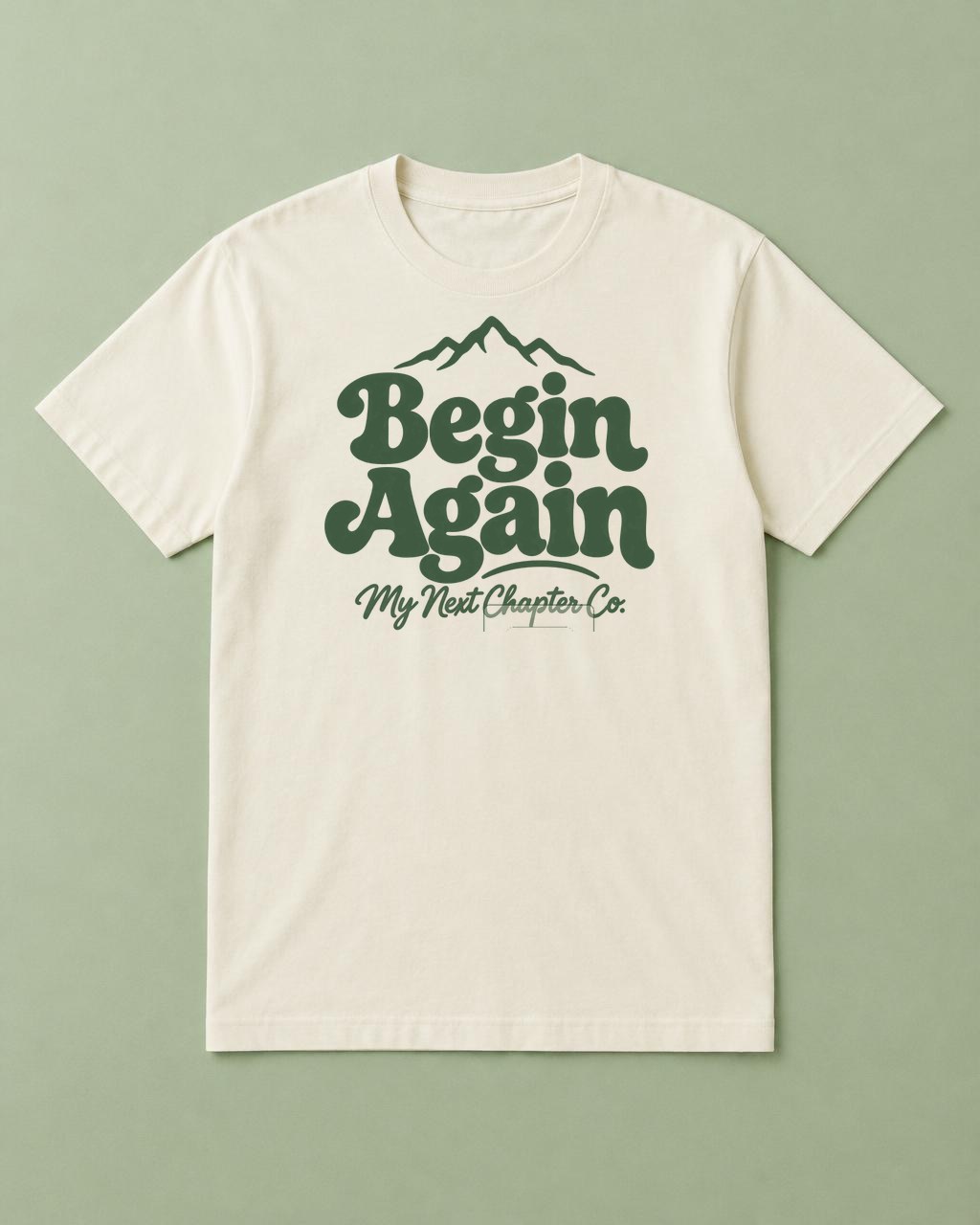 Cream shirt mockup printed with the exact supplied Begin Again artwork with green rounded lettering, a mountain outline, and My Next Chapter Co. beneath