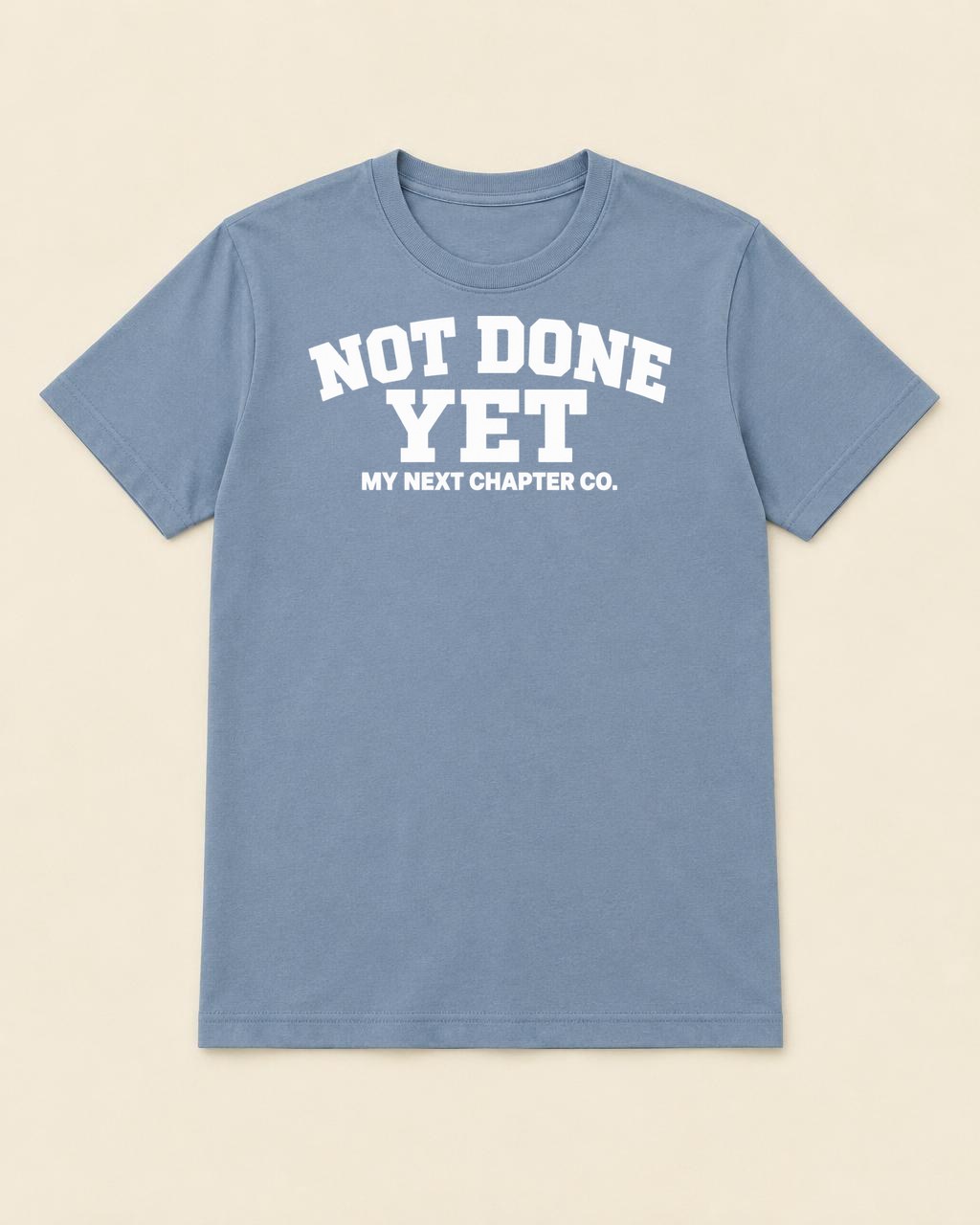 Dusty blue shirt mockup printed with the exact Not Done Yet artwork with white athletic lettering and My Next Chapter Co. beneath