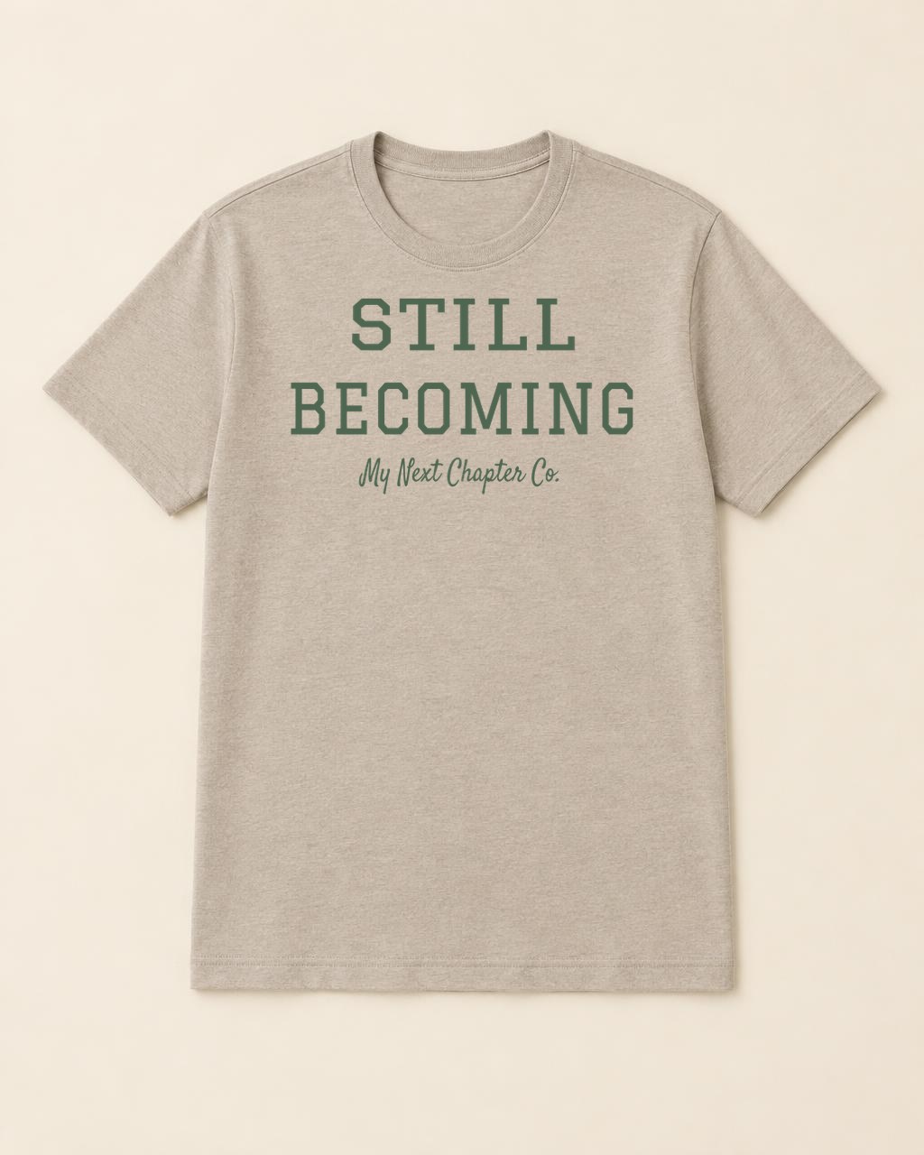 Taupe shirt mockup printed with the exact supplied Still Becoming artwork with green uppercase athletic lettering and My Next Chapter Co. beneath